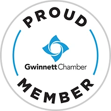 Circular badge with text “Proud Member” around a blue geometric logo and the words “Gwinnett Chamber” in the center.